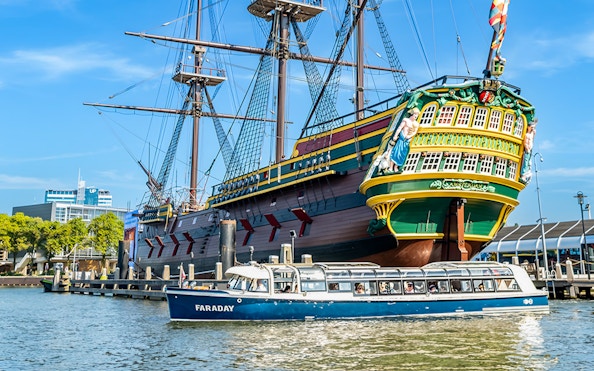 Canal cruise boat passing a historic ship in Amsterdam harbor.