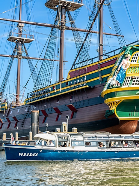 Canal cruise boat passing a historic ship in Amsterdam harbor.