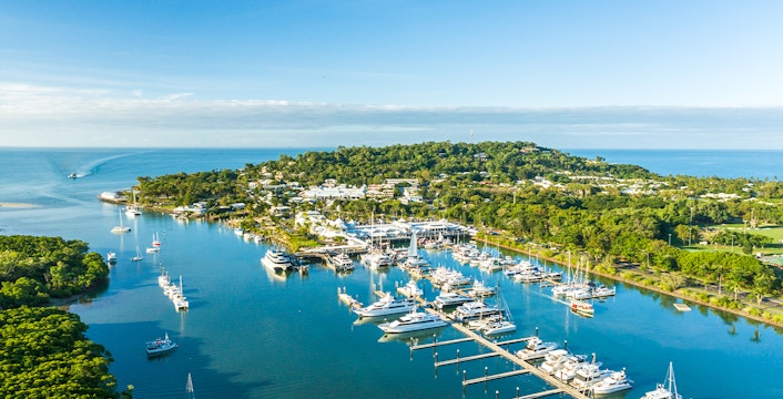 Port Douglas harbor with anchored sailboats and lush green hills in the background.
