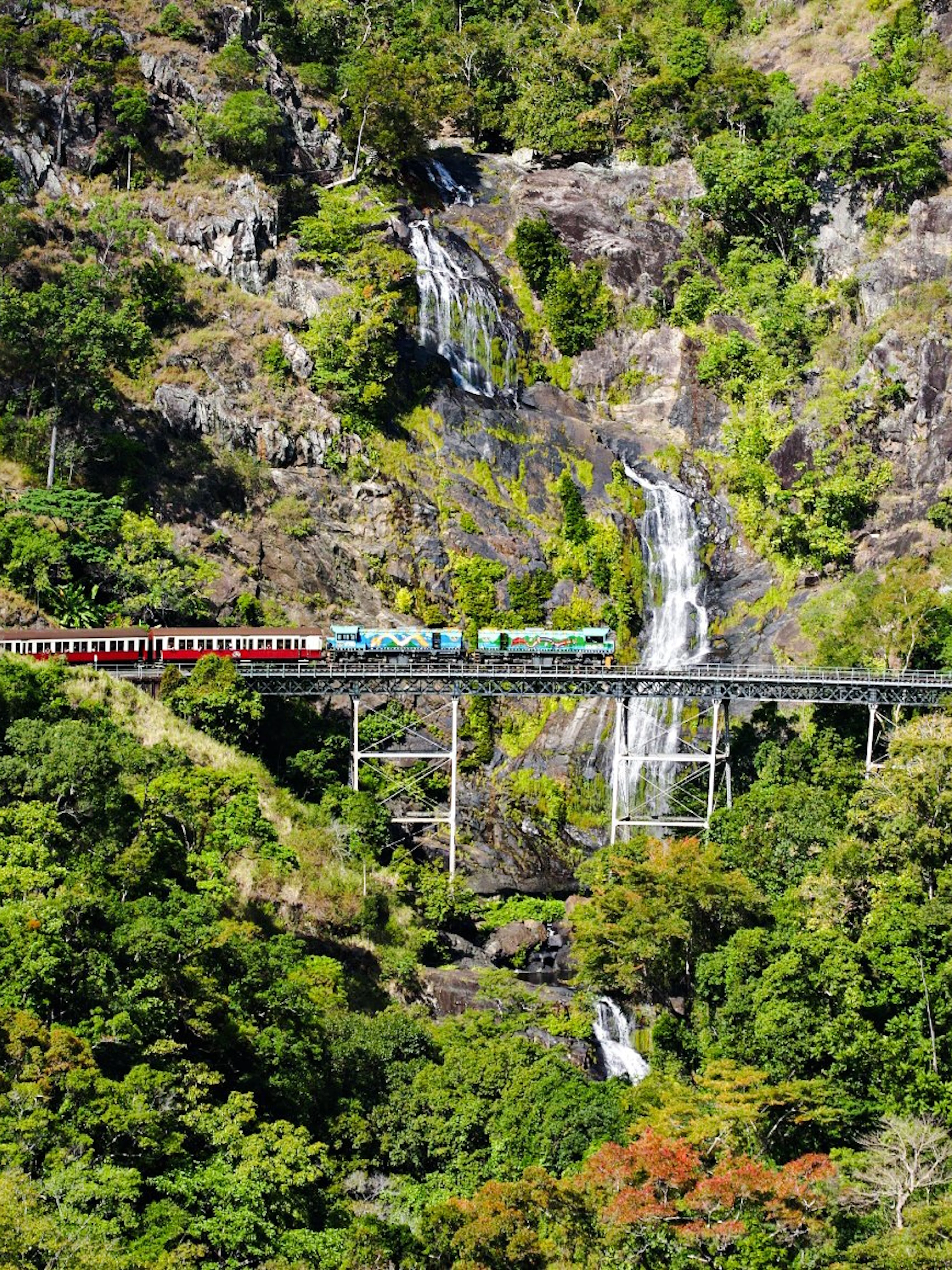 Train crossing a bridge with a waterfall in a lush forest during a scenic tour.