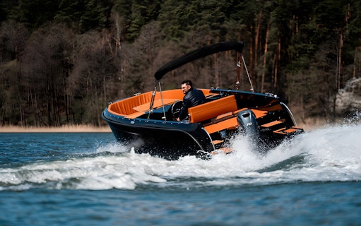 Boat speeding on Lake Como with a person steering, surrounded by forested hills.