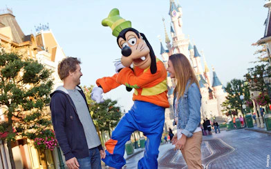 Guests interacting with Goofy at Disneyland Paris with Sleeping Beauty Castle in the background.