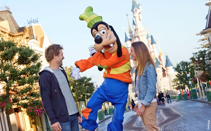 Guests interacting with Goofy at Disneyland Paris with Sleeping Beauty Castle in the background.