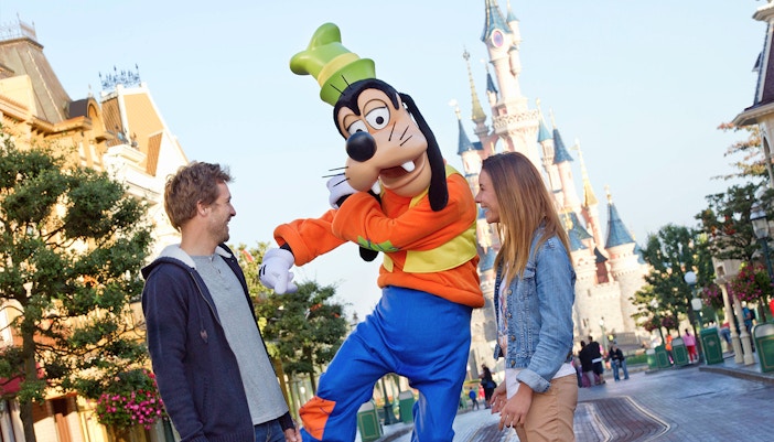 Guests interacting with Goofy at Disneyland Paris with Sleeping Beauty Castle in the background.