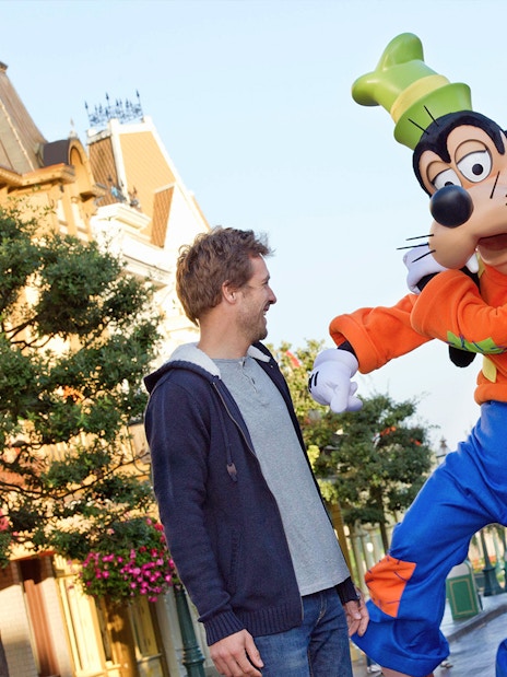 Guests interacting with Goofy at Disneyland Paris with Sleeping Beauty Castle in the background.