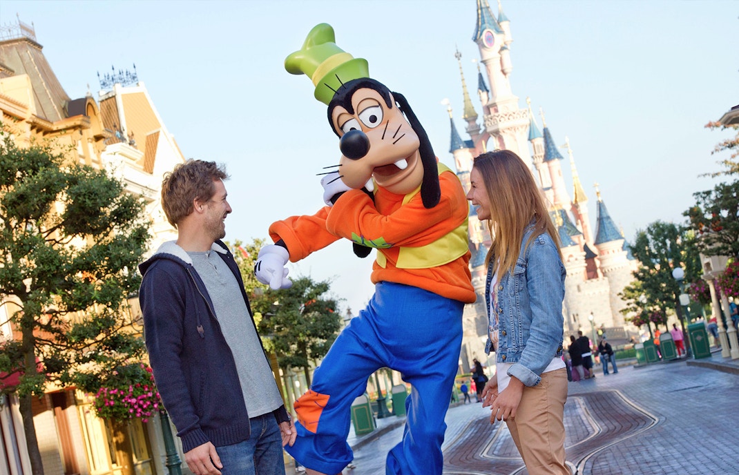 Guests interacting with Goofy at Disneyland Paris with Sleeping Beauty Castle in the background.