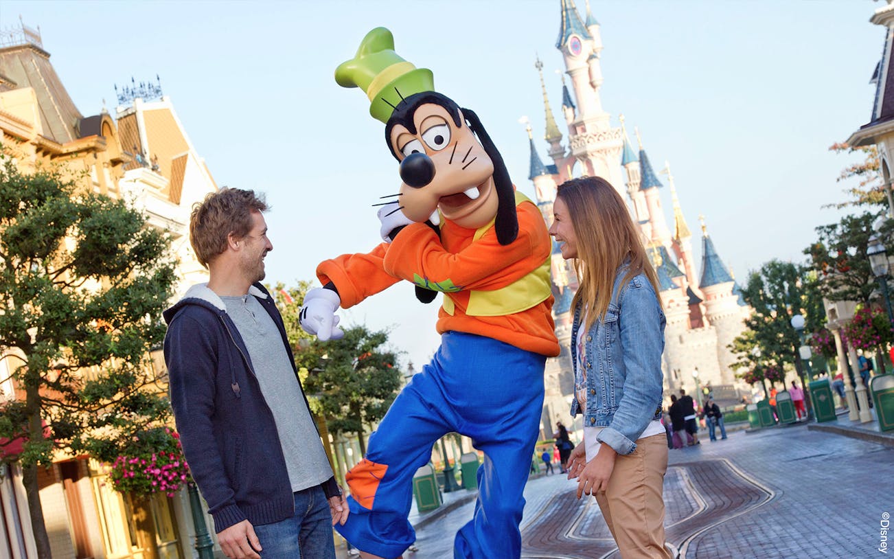 Guests interacting with Goofy at Disneyland Paris with Sleeping Beauty Castle in the background.