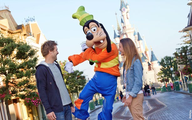 Guests interacting with Goofy at Disneyland Paris with Sleeping Beauty Castle in the background.