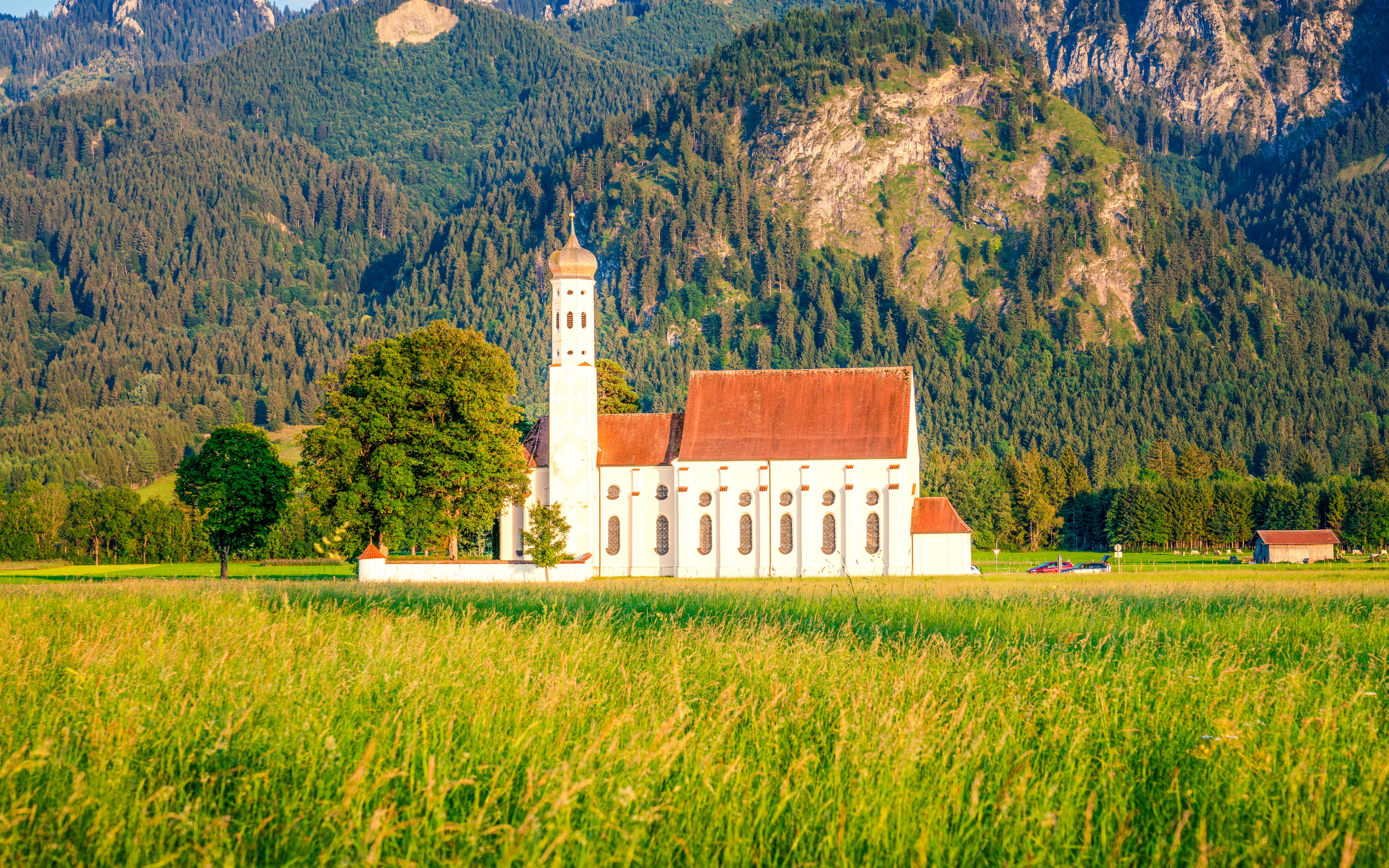 St. Coloman Church in a green field with mountain backdrop, Bavaria, Germany.