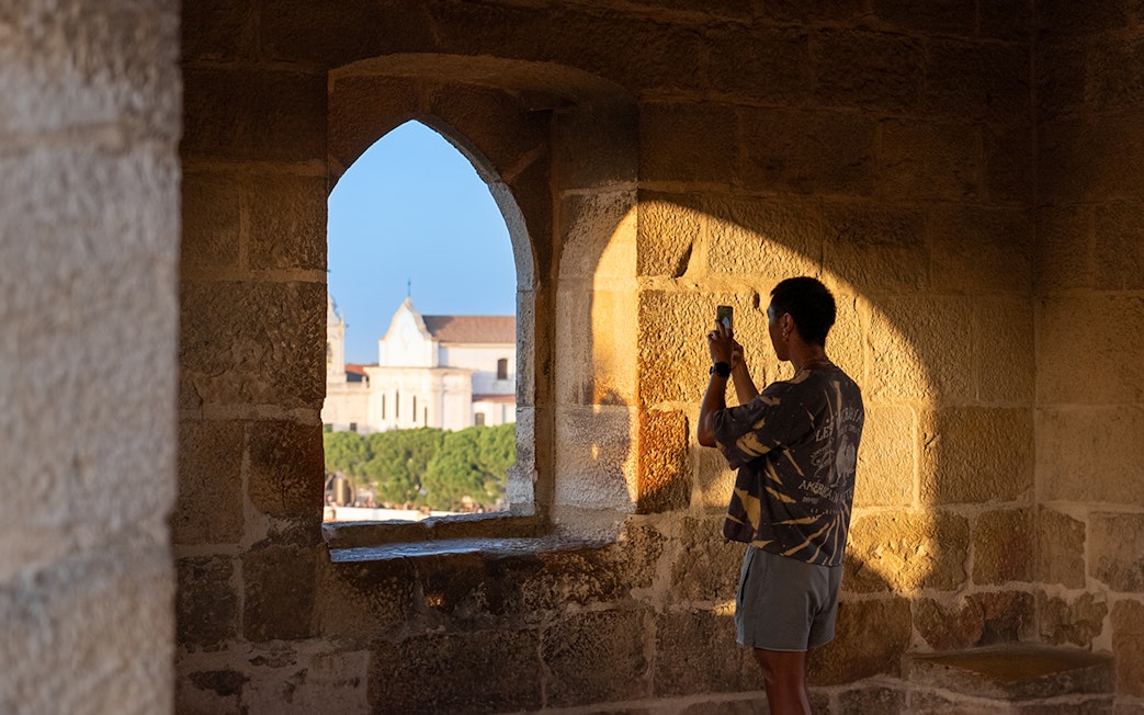 Visitor taking photo of St. George’s Castle through stone archway at sunset.