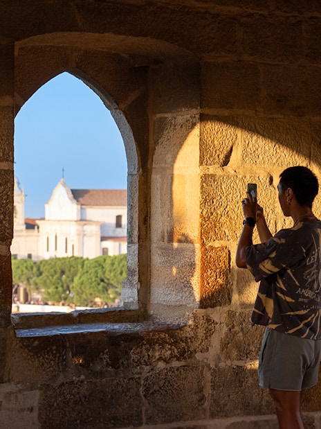 Visitor taking photo of St. George’s Castle through stone archway at sunset.