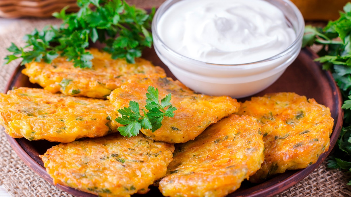 Pumpkin fritters with parsley garnish and a bowl of sour cream.