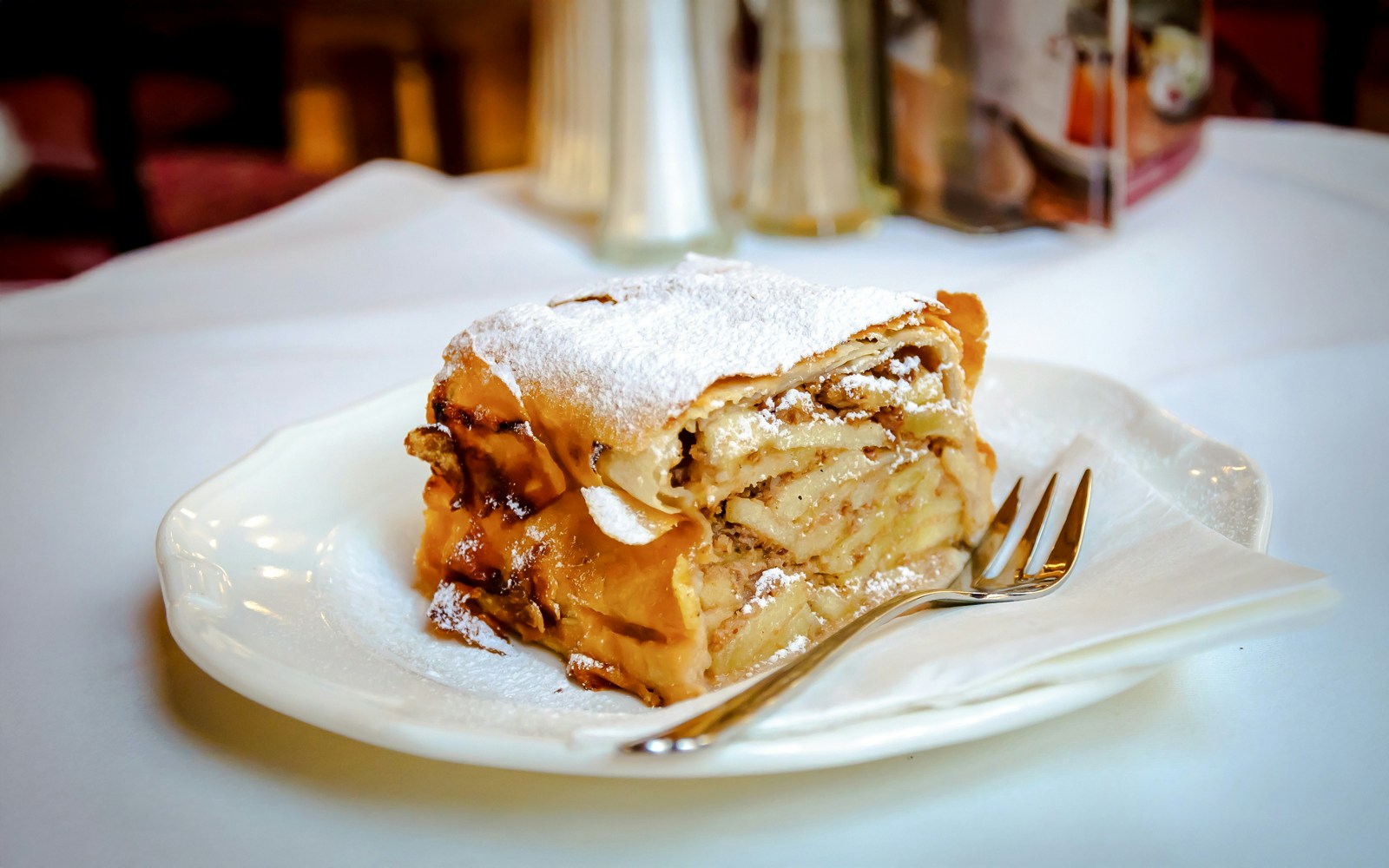 Slice of apple strudel with layers of apples and spices on a plate.