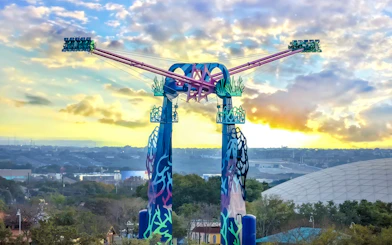 SeaWorld San Antonio ride with colorful towers and sunset backdrop.