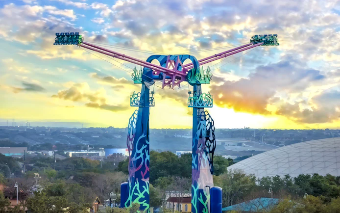 SeaWorld San Antonio ride with colorful towers and sunset backdrop.