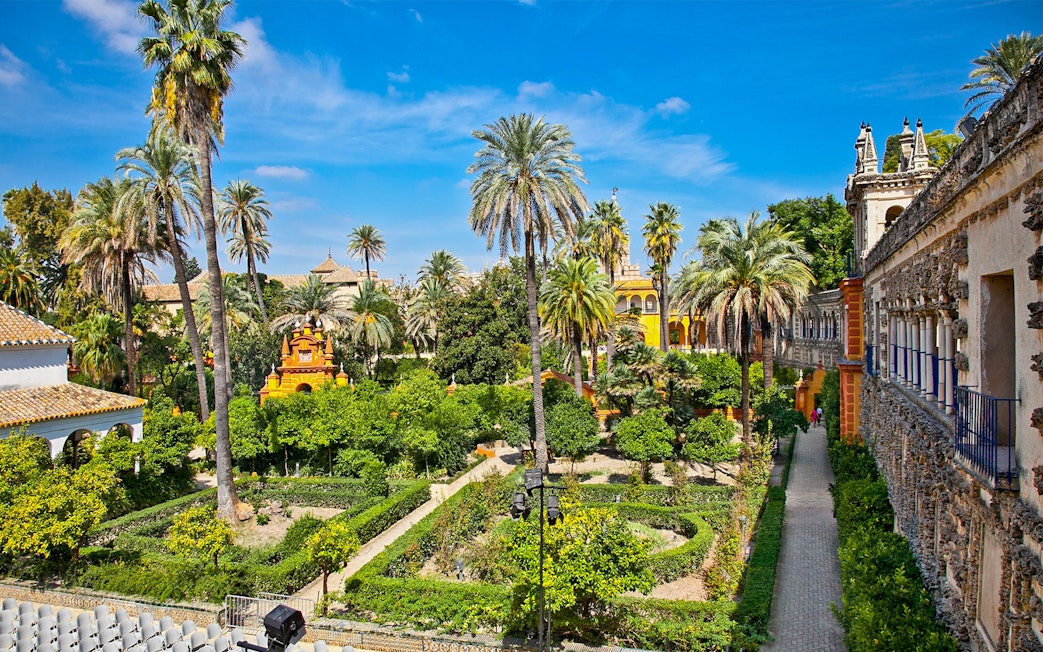 Alcazar of Seville gardens with palm trees and historic architecture.