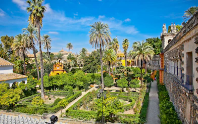 Alcazar of Seville gardens with palm trees and historic architecture.