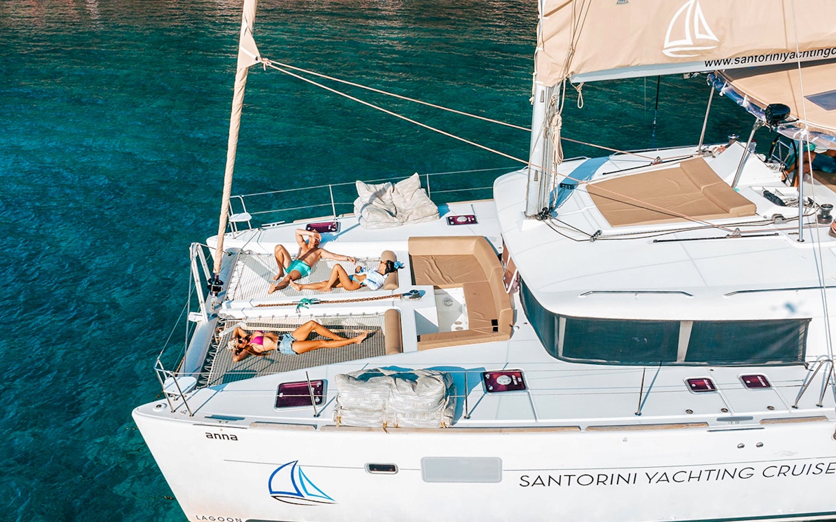 Catamaran with people sunbathing on deck, Santorini Luxury Cruise.
