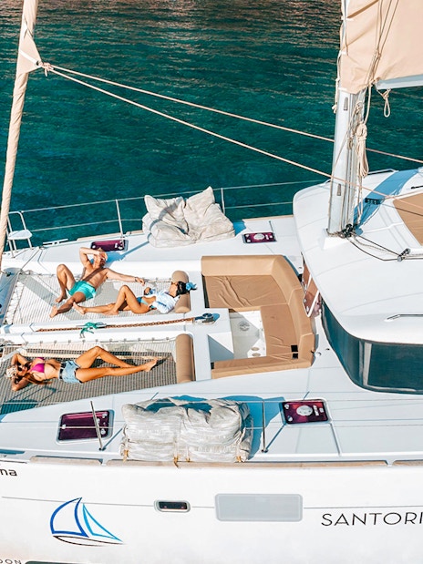 Catamaran with people sunbathing on deck, Santorini Luxury Cruise.