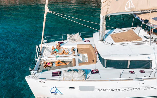 Catamaran with people sunbathing on deck, Santorini Luxury Cruise.