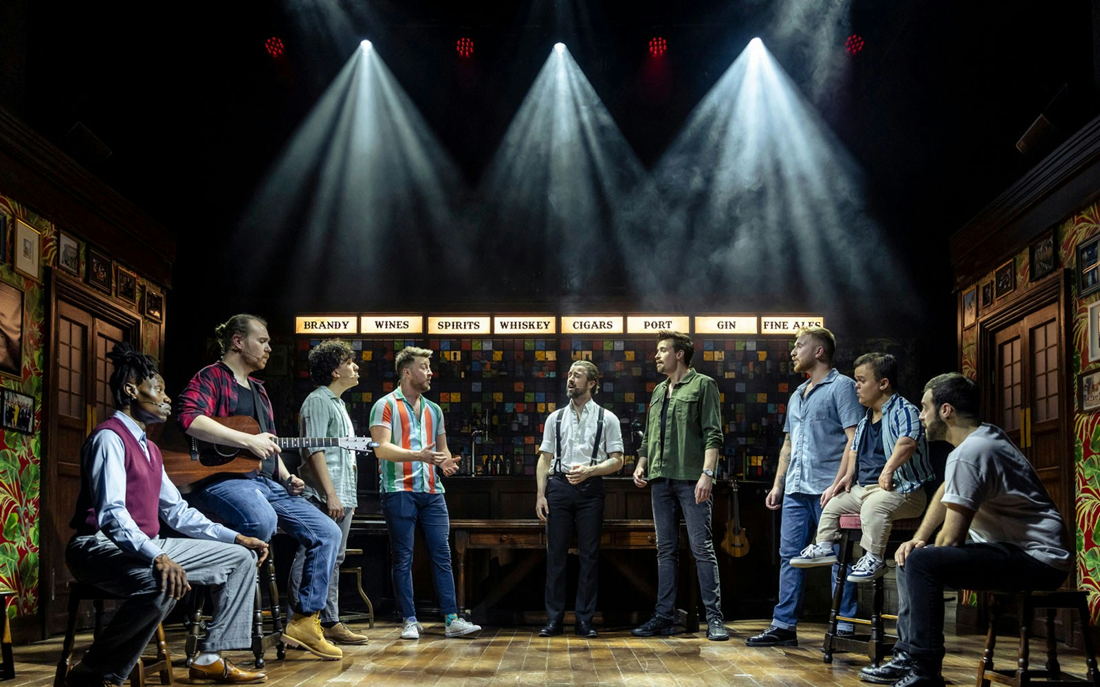 Performers on stage during The Choir of Man show, with bar backdrop and spotlights.