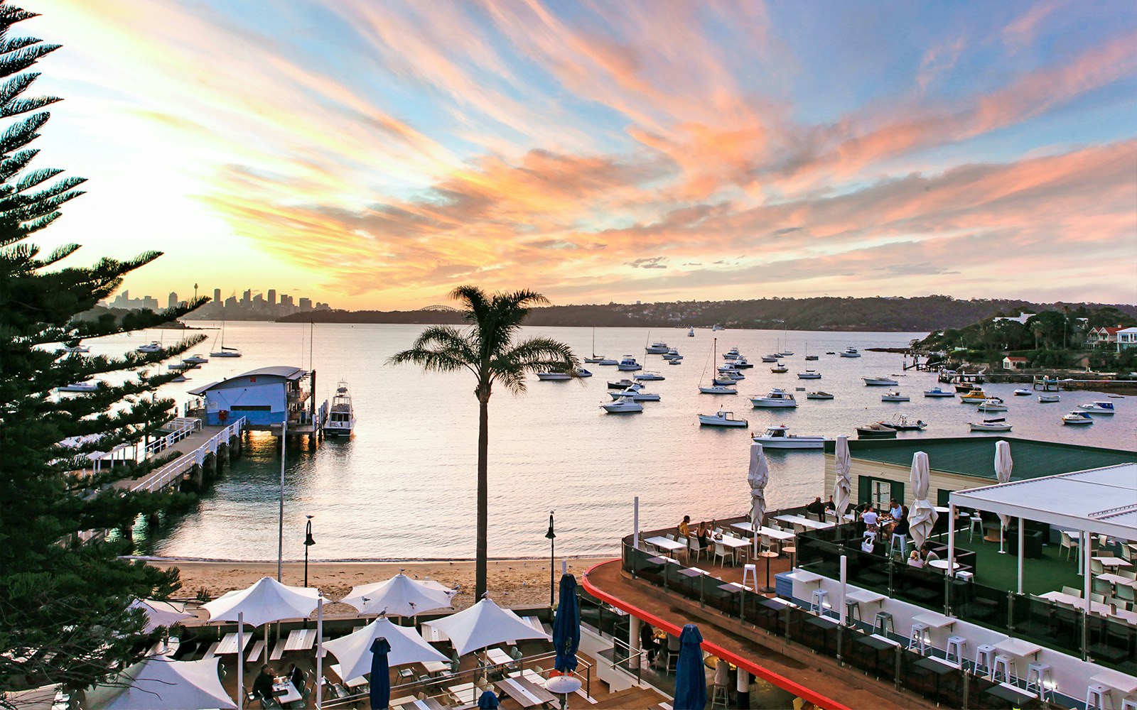 Sydney Harbour view with boats and city skyline at sunset, seen from a waterfront dining area.