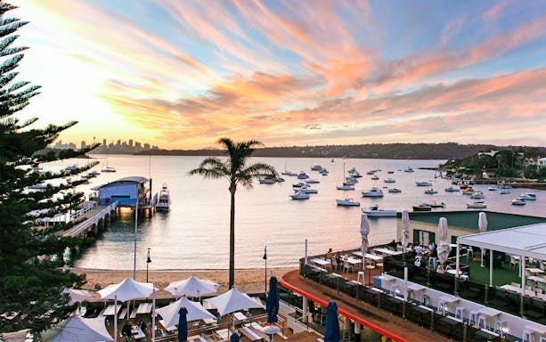 Sydney Harbour view with boats and city skyline at sunset, seen from a waterfront dining area.