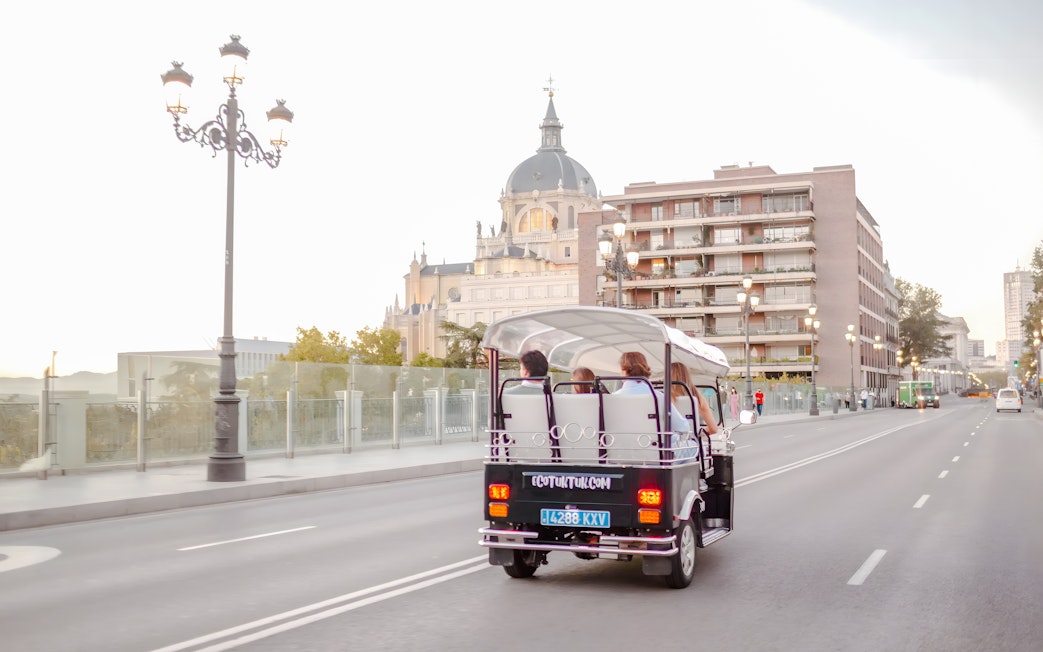 Electric tuk-tuk driving near Almudena Cathedral in Madrid, Spain.