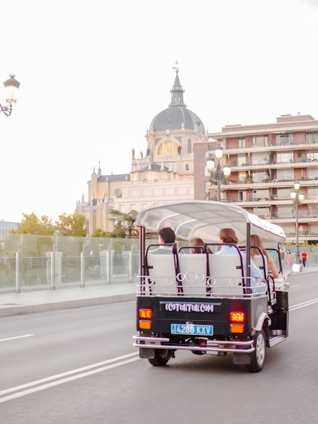 Electric tuk-tuk driving near Almudena Cathedral in Madrid, Spain.