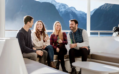 Group enjoying drinks on a Milford Sound cruise with scenic mountain views.