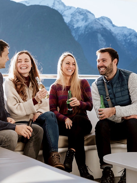 Group enjoying drinks on a Milford Sound cruise with scenic mountain views.