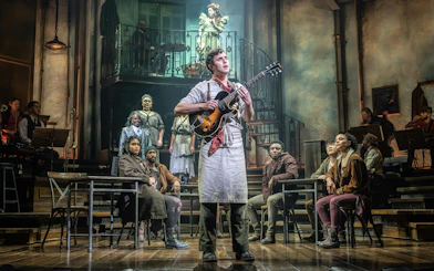 Performer with guitar on stage during Hadestown show, West End.
