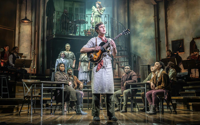 Performer with guitar on stage during Hadestown show, West End.