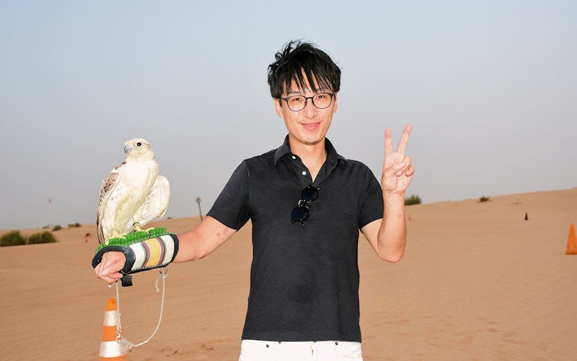 Man holding a falcon in a desert setting.
