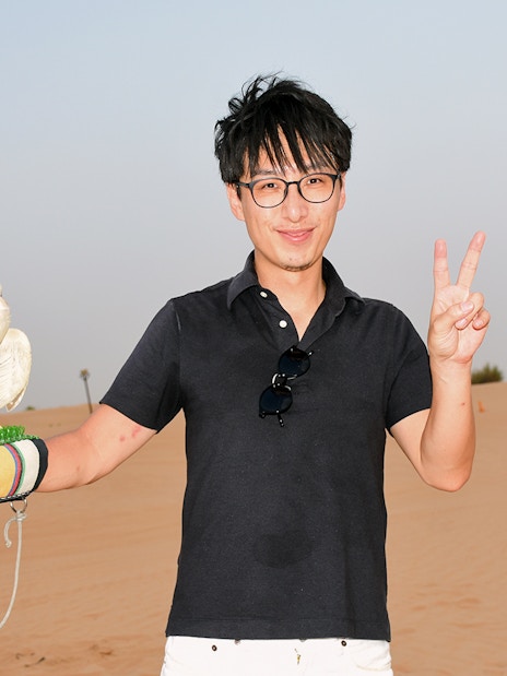 Man holding a falcon in a desert setting.