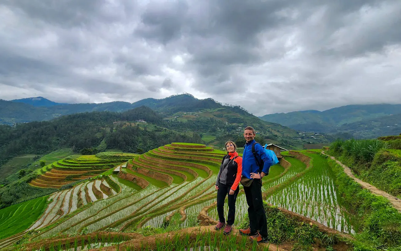 Trekking couple on Mu Cang Chai terraced rice fields with mountains in the background.