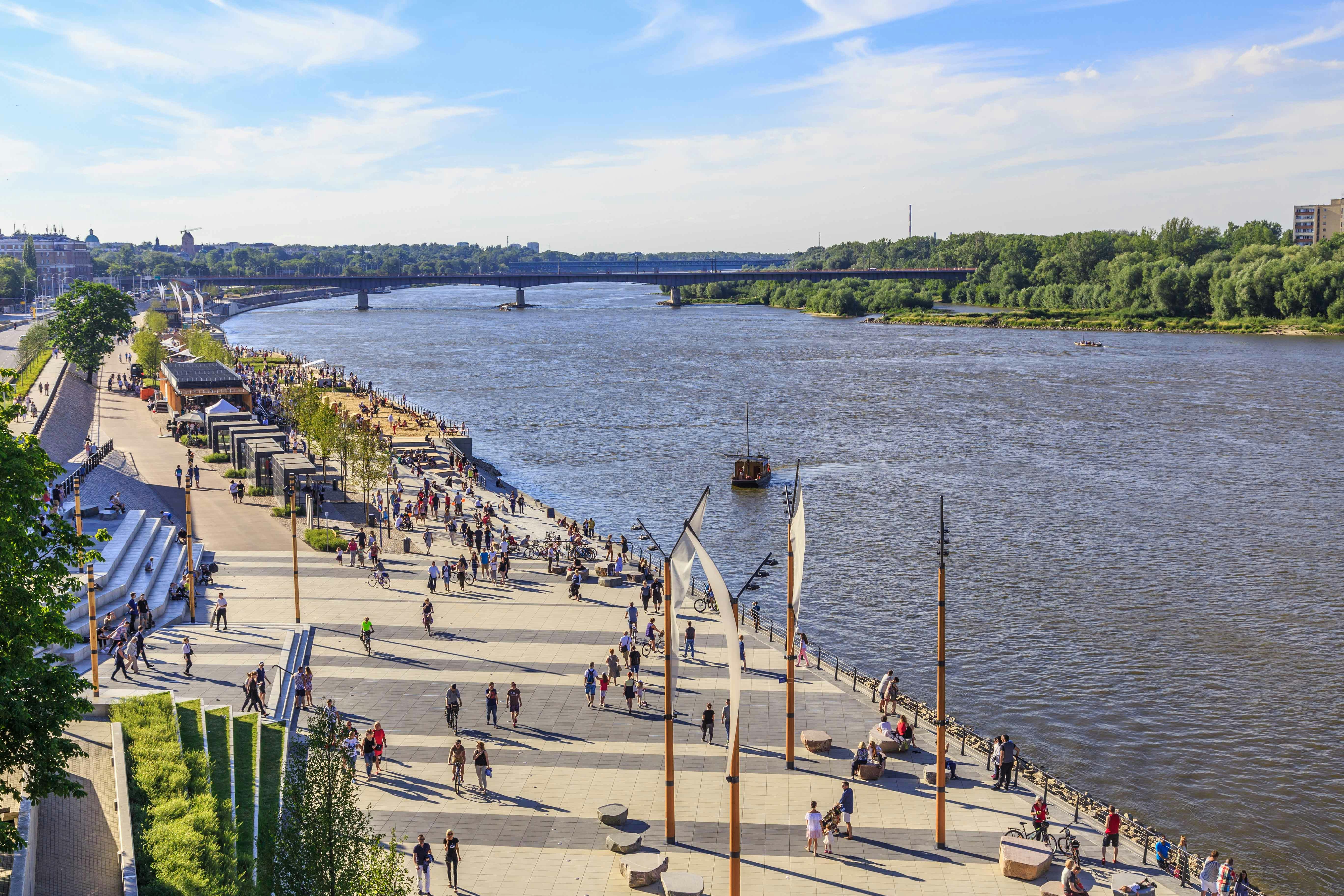People walking and cycling along the Vistula Boulevards in Warsaw, Poland, near the river.