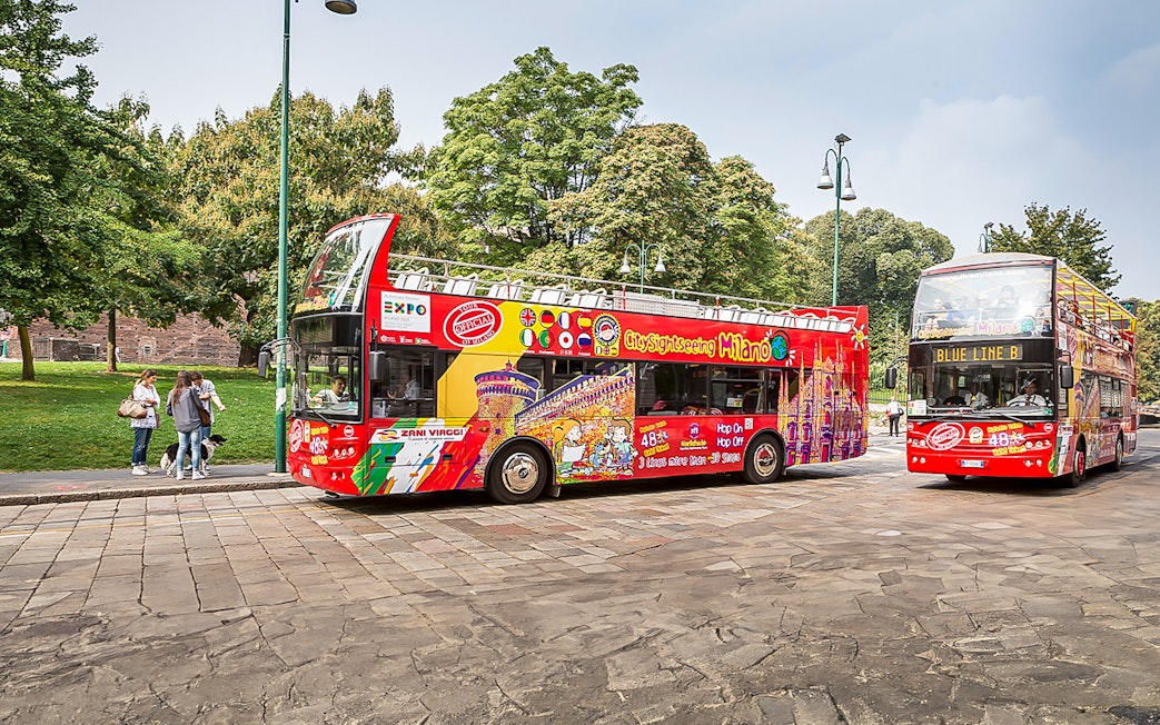 City Sightseeing buses in Milan near a park with trees in the background.