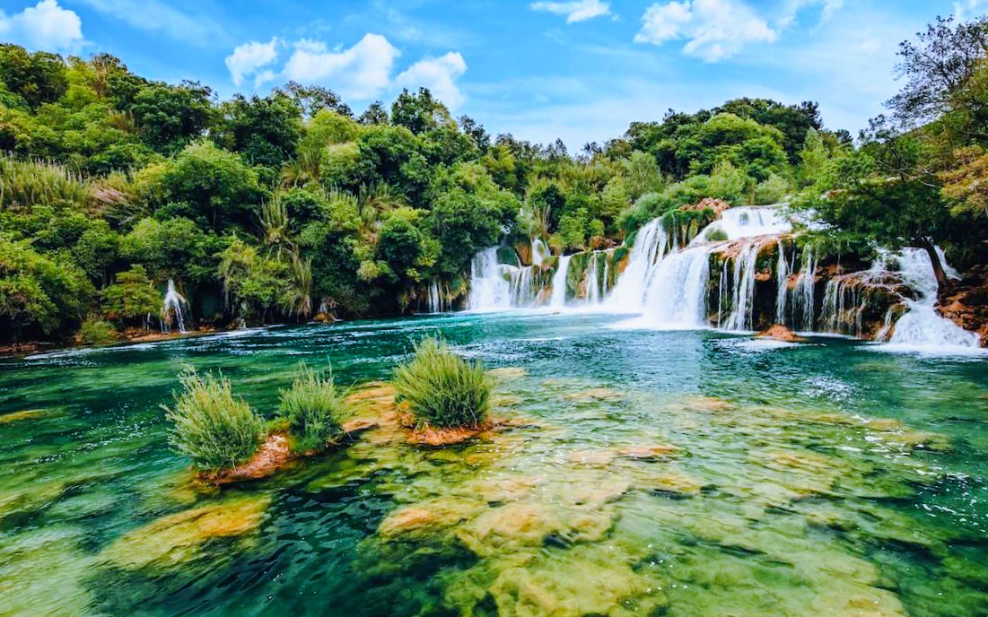 Waterfall flowing into a clear pool surrounded by lush greenery in Krka National Park, Croatia.