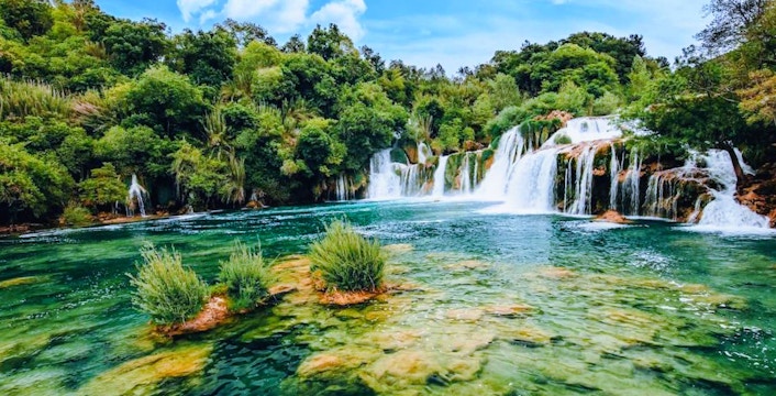 Waterfall flowing into a clear pool surrounded by lush greenery in Krka National Park, Croatia.
