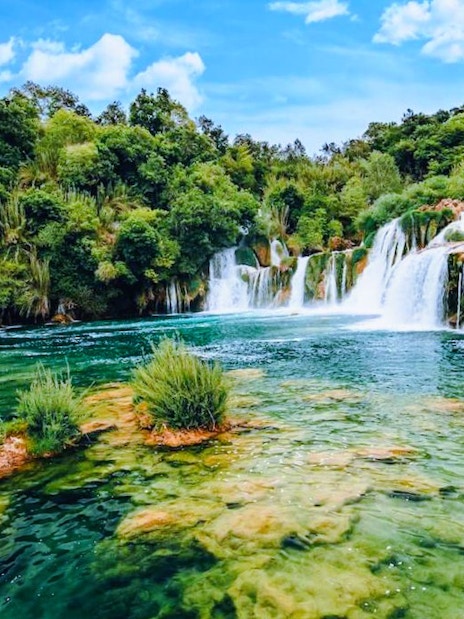 Waterfall flowing into a clear pool surrounded by lush greenery in Krka National Park, Croatia.