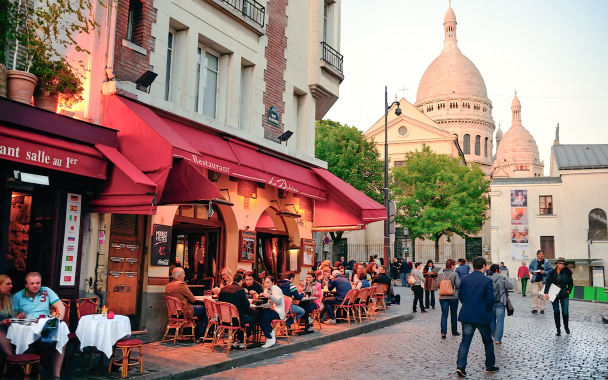 Outdoor dining at a restaurant in Montmartre, Paris, with Sacré-Cœur Basilica in the background.