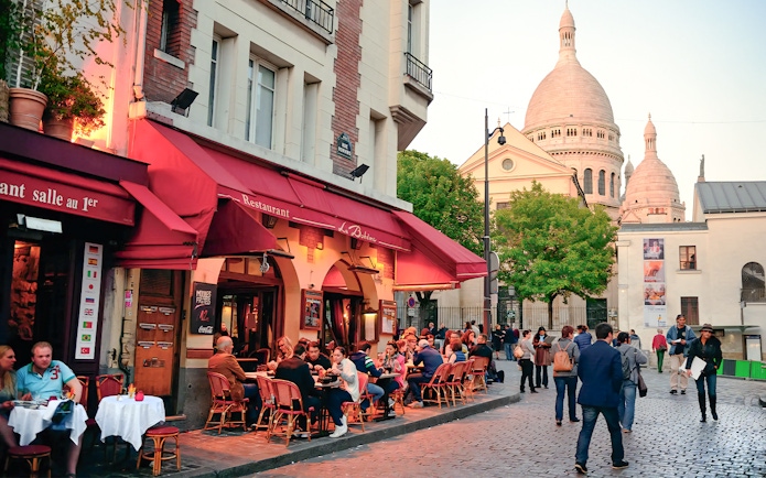 Outdoor dining at a restaurant in Montmartre, Paris, with Sacré-Cœur Basilica in the background.