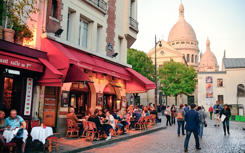 Outdoor dining at a restaurant in Montmartre, Paris, with Sacré-Cœur Basilica in the background.