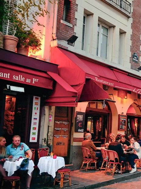 Outdoor dining at a restaurant in Montmartre, Paris, with Sacré-Cœur Basilica in the background.