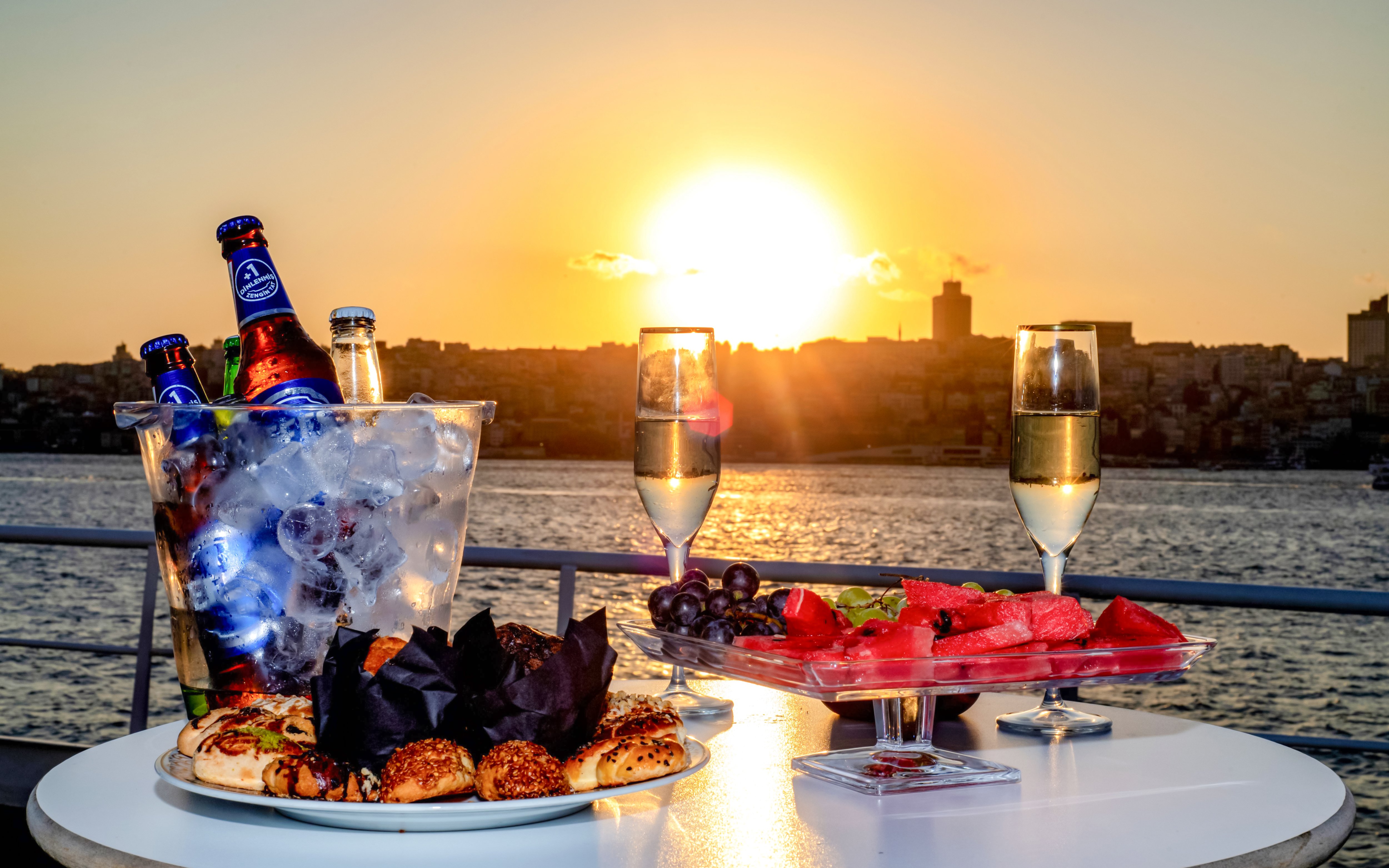 Bosphorus sunset cruise with champagne, fruit platter, and pastries on a table.