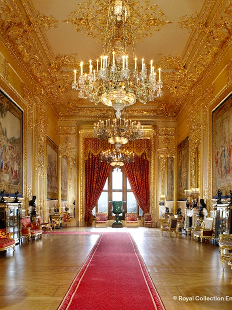 Windsor Castle interior with ornate chandeliers, gilded walls, and red carpet.