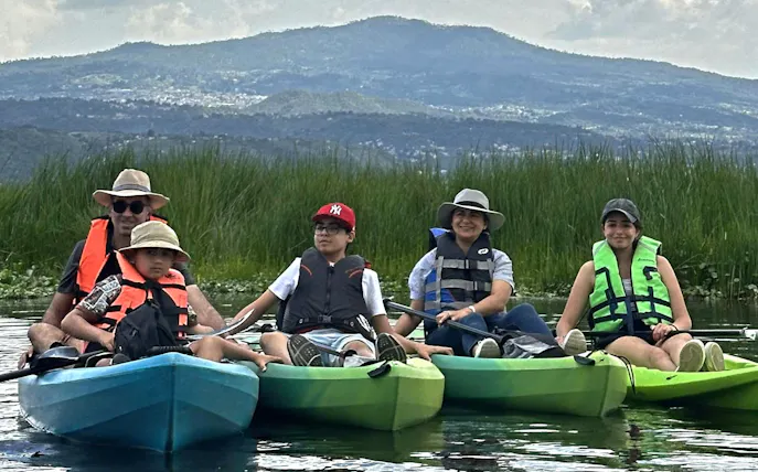 Group kayaking on Xochimilco canal with local guide, surrounded by lush greenery.