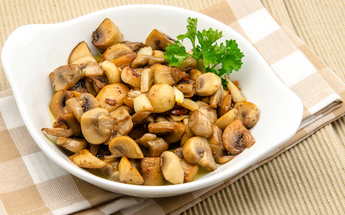 Sautéed mushrooms with parsley garnish on a white dish, featured in St. Georg kulinarisch food tour.