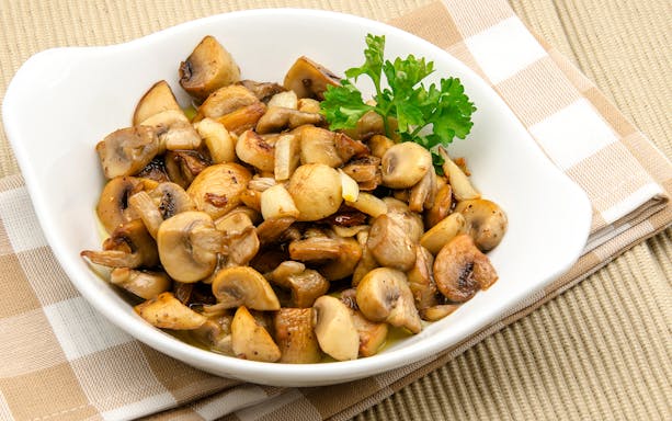 Sautéed mushrooms with parsley garnish on a white dish, featured in St. Georg kulinarisch food tour.